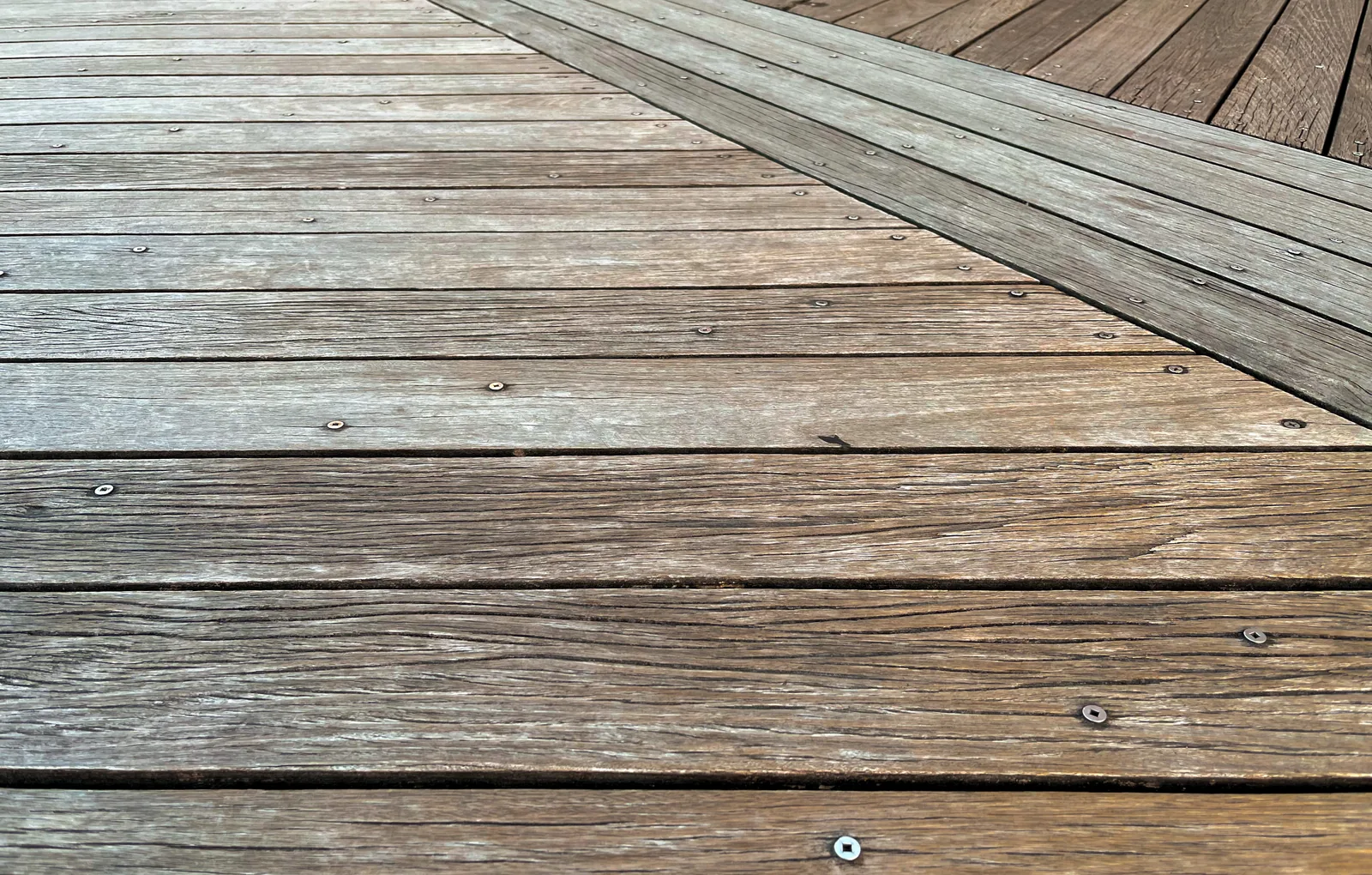 Weathered grey deck boards running at an angle with visible screw heads